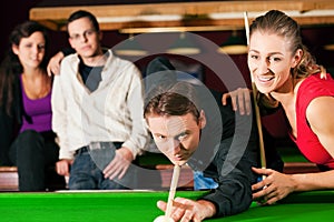 Group of four friends in a billiard hall playing s