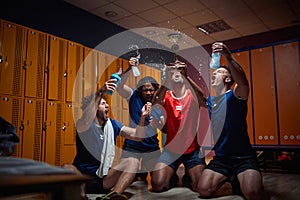 Group of four men team players in locker room celebrating success together, holding golden medal and screeming of joy, splashing photo