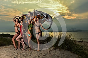 Group of four models wearing bikinis posing at sunset beach.