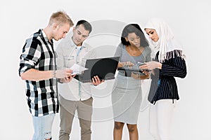 Group Of Four Multi Ethnic Students, working studying together, using laptop and tablet, standing On White Background