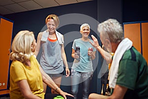 Group of four people in dressing room preparing for workout, senior man high fiving senior woman