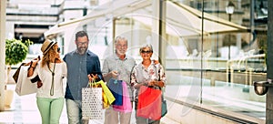 Group of four people going shopping together holding shopping bags with presents or gifts for christmas - buying clothes and more