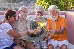 Group of four people and seniors sitted on a bench together playing and celebrating something with fire or sparklers - party or