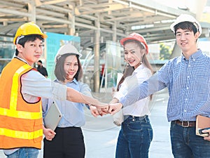 Group of four young Asian male and female engineers wearing safety vest and helmet, putting hands join together at outside office