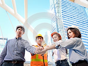 Group of four young Asian male and female engineers wearing safety vest and helmet, putting hands join together at outside office