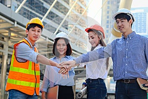 Group of four young Asian male and female engineers wearing safety vest and helmet, putting hands join together at outside office