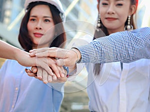 Group of four young Asian male and female engineers wearing safety vest and helmet, putting hands join together at outside office