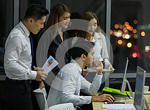 Group of four youthful Asian male and female colleagues with cute smiling gathered in front of a computer to planning their