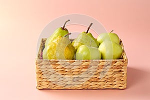 Group of fresh, ripe and juicy apples and pears in a water hyacinth basket against pink background