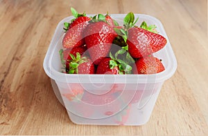 Group of fresh, ripe red strawberries with green leaves in plastic container