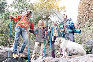 Group of friends with backpacks doing trekking excursion on mountain with their pet