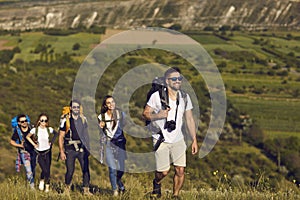 A group of friends with backpacks on a hike in nature. Young people tourists are walking on a hill in the mountains.