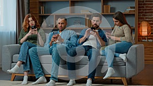 Group friends business people sit on couch with mobile phones chatting in social media ignoring each other multiethnic