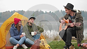 Group of friends camping.They are sitting around camp fire, playing guitar