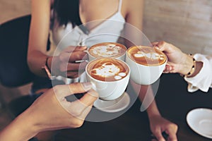 Group of friends cheers with latae cup in cafe bar with phone on table sitting intdoor at cafe - Young girl group having fun photo