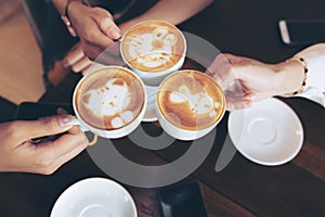 Group of friends cheers with latae cup in cafe bar with phone on table sitting intdoor at cafe - Young girl group having fun photo