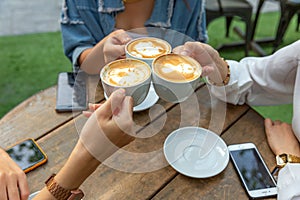 Group of friends cheers with latae cup in cafe bar with phone on table sitting outdoor at cafe - Young girl group having fun photo
