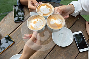 Group of friends cheers with latae cup in cafe bar with phone on table sitting outdoor at cafe - Young girl group having fun