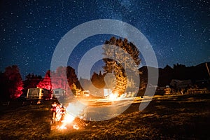 Group of friends chill and warm near a bonfire in camping during a hiking trip.