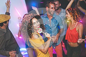 Group of friends dancing and drinking champagne at nightclub - Young happy people having fun and enjoying party eating candy