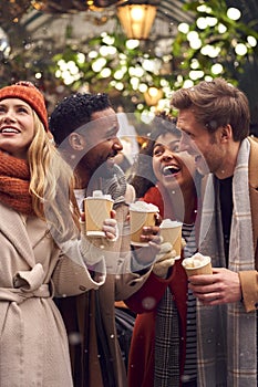 Group Of Friends Drinking Hot Chocolate With Marshmallows In Snow At Outdoor Christmas Market