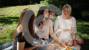 Group of friends eating healthy in nature on a sunny summer day, picnic ham sandwiches in a basket