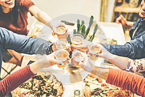 Group of friends enjoying dinner toasting with beers and eating take away pizza at home - Cheers of happy people drinking beer