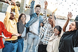 Group of friends enjoying party throwing confetti in the air - Young people having fun outside on urban weekend festival event
