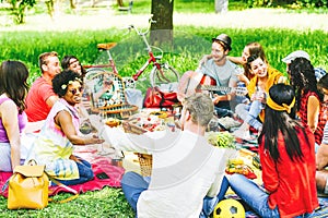 Group of friends enjoying a picnic while eating and drinking red wine sitting on blanket in a park outdoor