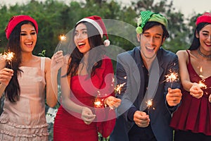 Group of friends enjoying with sparklers in the party. Selective focus on face of woman in red dress