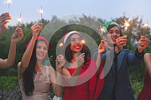 Group of friends enjoying with sparklers in the party. Selective focus on face of woman in red dress