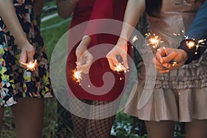 Group of friends enjoying with sparklers in the party. Selective focus on face of woman in red dress