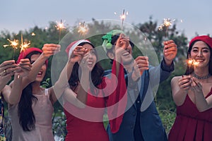 Group of friends enjoying with sparklers in the party. Selective focus on face of woman in red dress