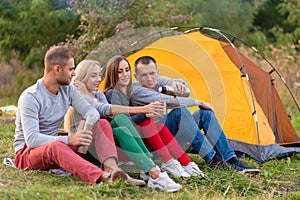 A group of friends is enjoying a warming drink from a thermos, on a cool evening by a fire in the forest. Fun time camping with