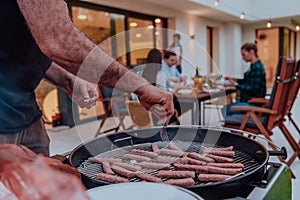 A group of friends and family barbecue together in the evening on the terrace in front of a large modern house