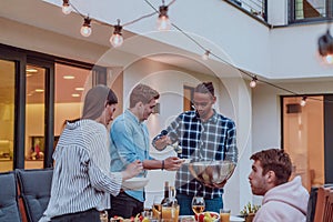 A group of friends and family barbecue together in the evening on the terrace in front of a large modern house