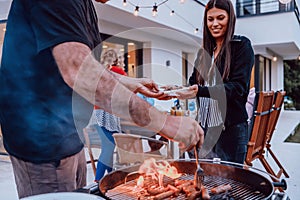 A group of friends and family barbecue together in the evening on the terrace in front of a large modern house