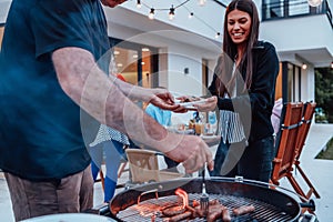 A group of friends and family barbecue together in the evening on the terrace in front of a large modern house