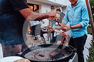 A group of friends and family barbecue together in the evening on the terrace in front of a large modern house