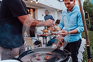 A group of friends and family barbecue together in the evening on the terrace in front of a large modern house