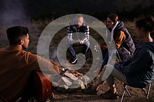 Group of friends gathering around bonfire at camping site in evening