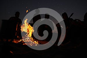 Group of friends gathering around bonfire at night. Camping season