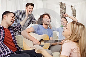 A group of friends with a guitar sing songs at a party indoor