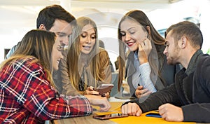 Group of friends hanging out with each other sitting in a bar using their mobile phones - Young people , millennial holding