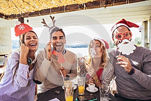 Group of friends having fun in cafe holding artificial mustache and lips stick