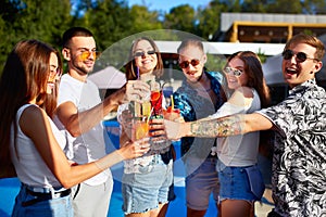 Group of friends having fun at poolside summer party clinking glasses with summer cocktails on sunny day near swimming