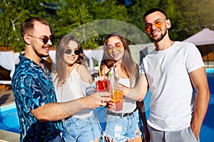 Group of friends having fun at poolside summer party clinking glasses with summer cocktails on sunny day near swimming