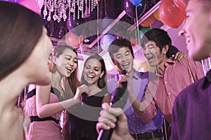 Group of friends holding microphones in a nightclub and singing together karaoke