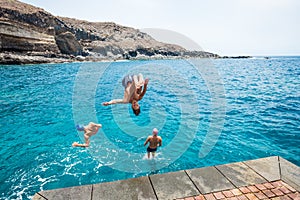 Group of friends jumping off together at the beach doing flips and having fun in the water - people enjoyinng thei holiday at the