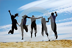 Group of friends jumps on sand, rear view